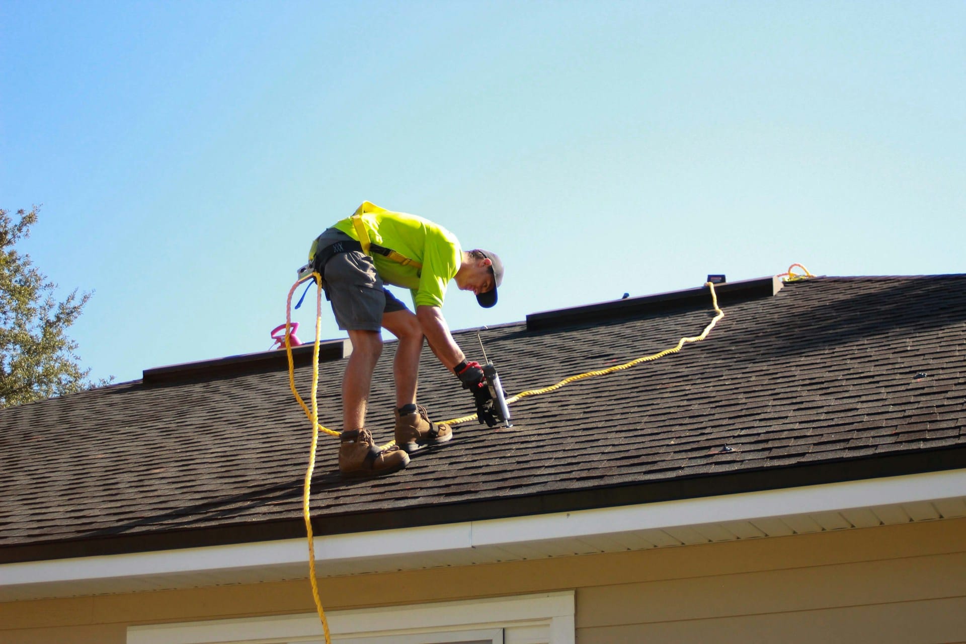 Roofing professional installing shingles on residential roof using safety harness and equipment