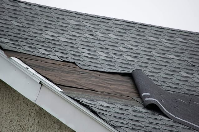Damaged roof shingles lifted by storm winds showing exposed underlayment