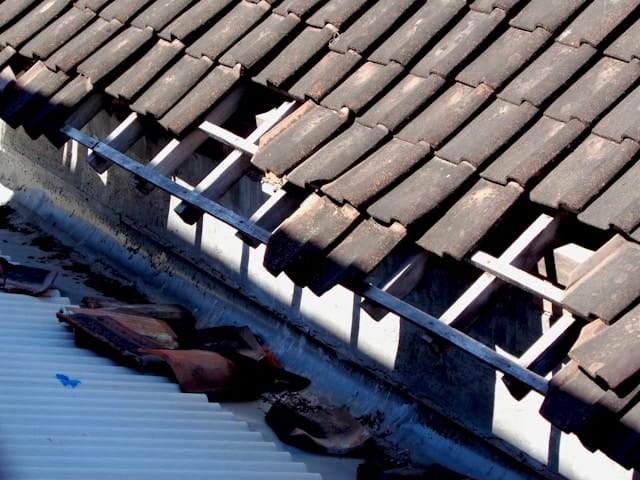 Storm damaged roof with missing tiles and exposed roof structure Storm damaged roof with missing tiles and exposed roof structure