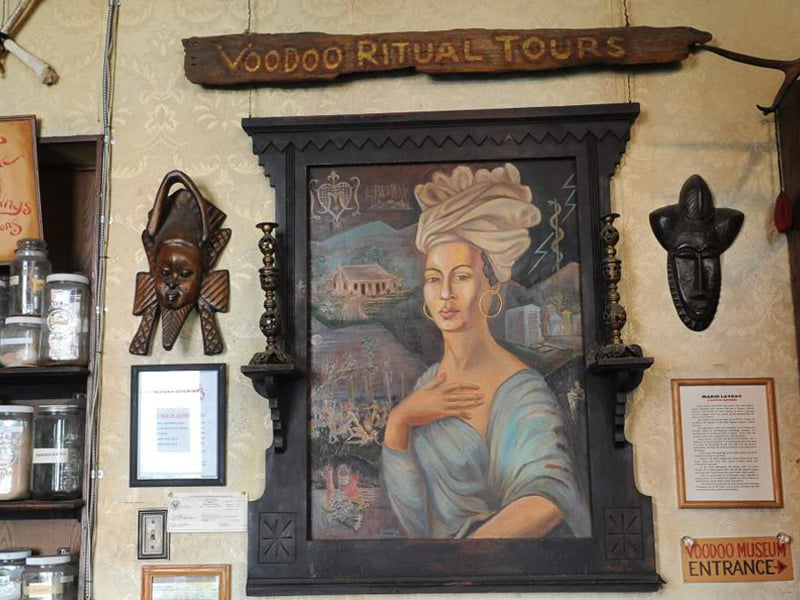A wall of art under a sign for Voodoo Ritual Tours at the Voodoo Museum