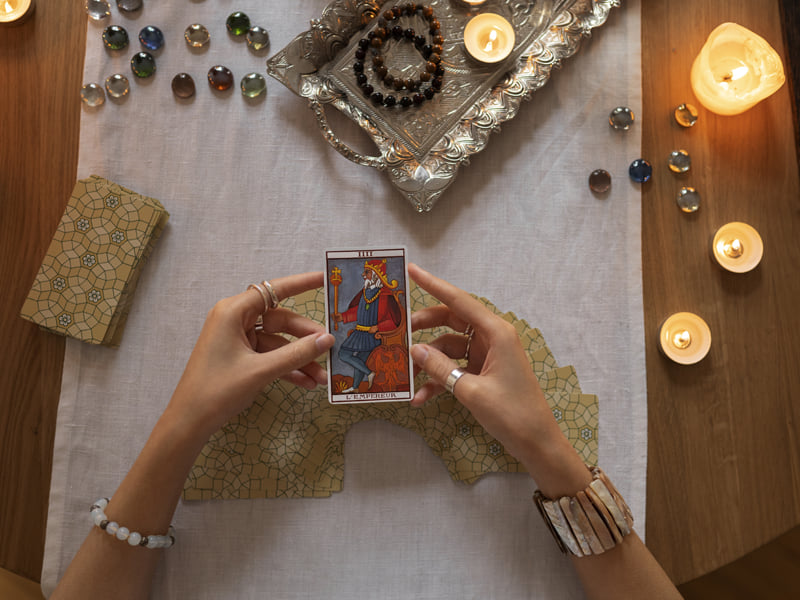 Young hands holding the emperor card from a tarot deck over a wooden table